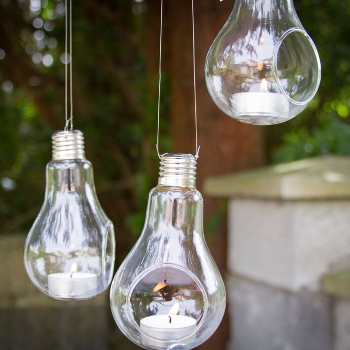Lit candles inside hanging light bulbs outdoors